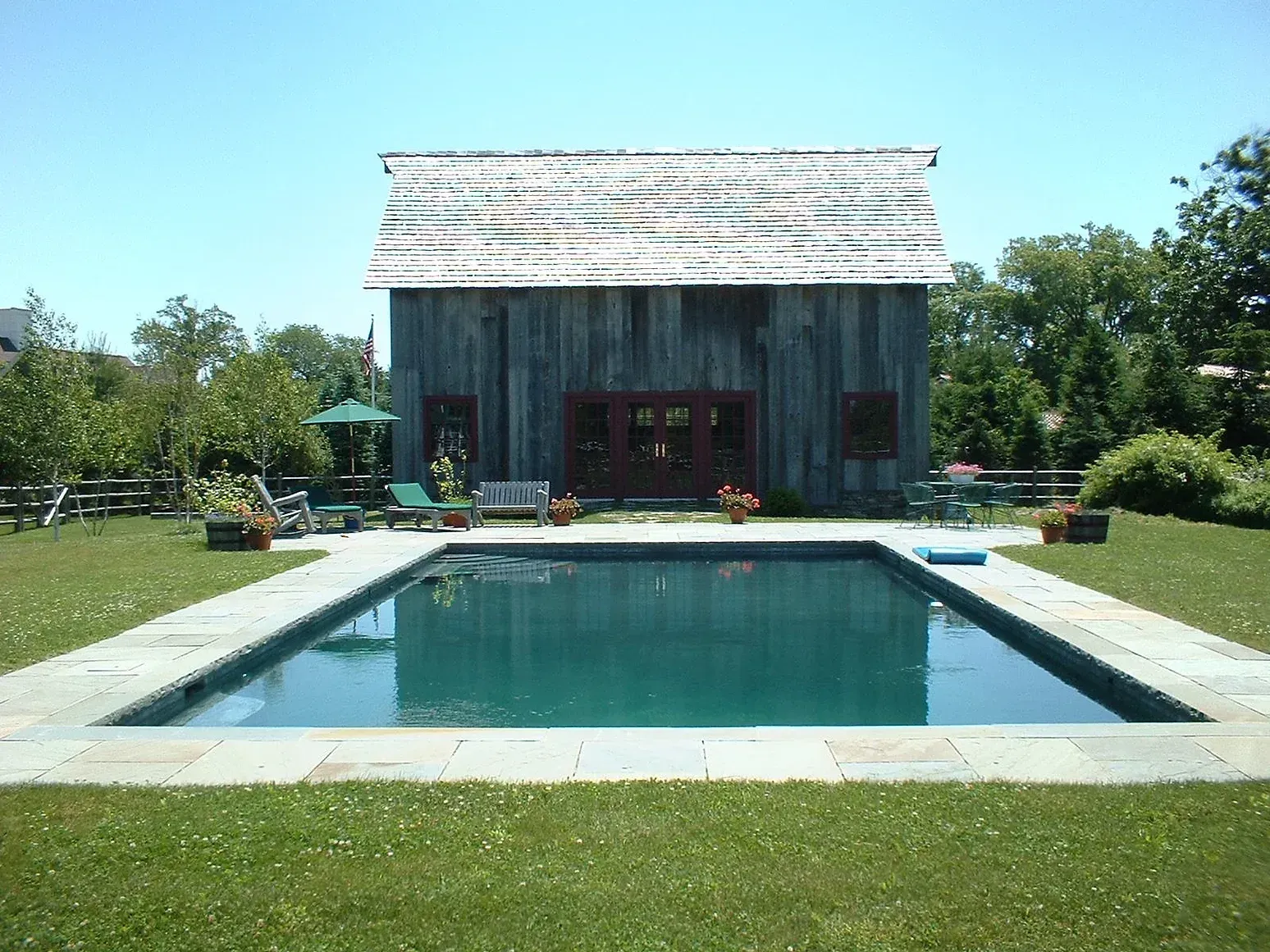 Swimming pool in a grassy backyard with a weathered wooden barn-like structure behind it.