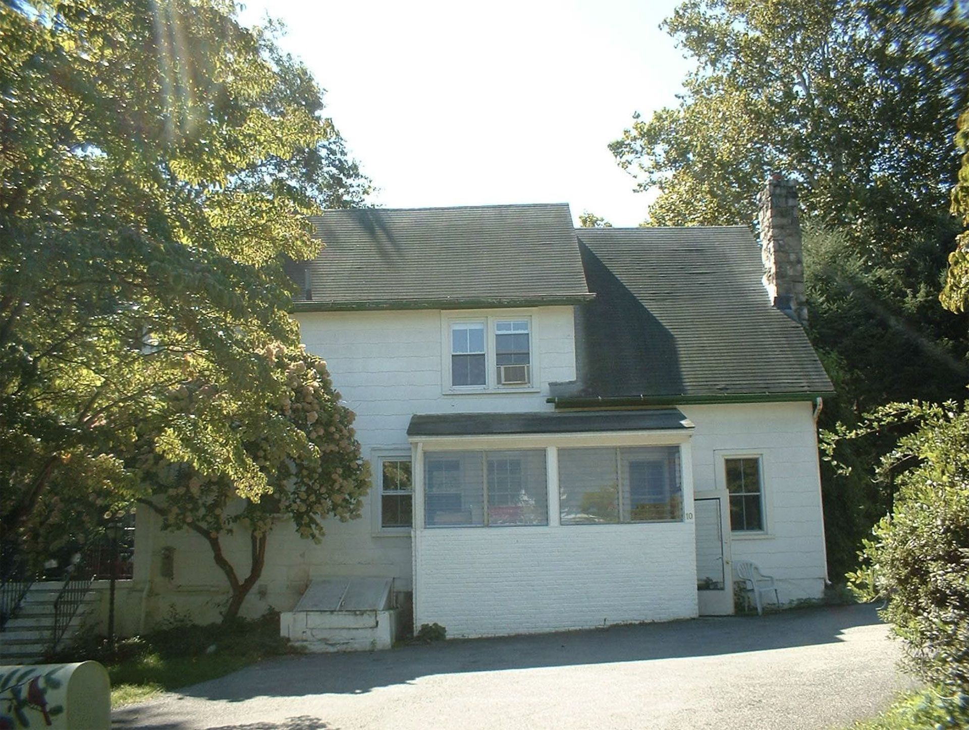 White house with dark roof and porch, surrounded by trees.