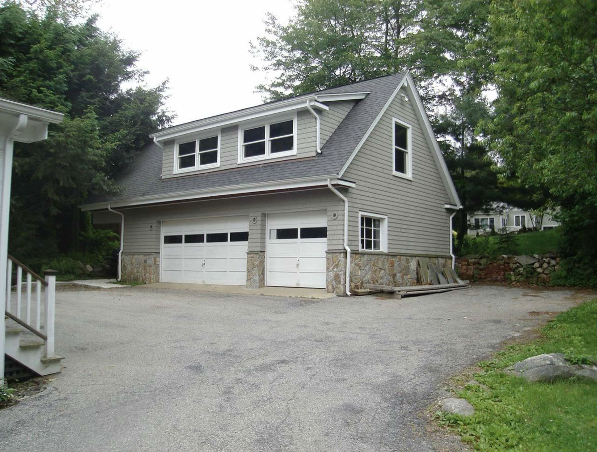 Two-car garage with gray siding, stone accents, and a second-story apartment, viewed from a gravel driveway.