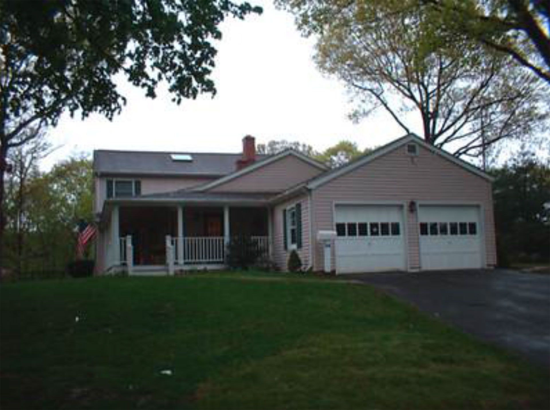 Pink house with two-car garage, porch, and American flag on a green lawn with surrounding trees.