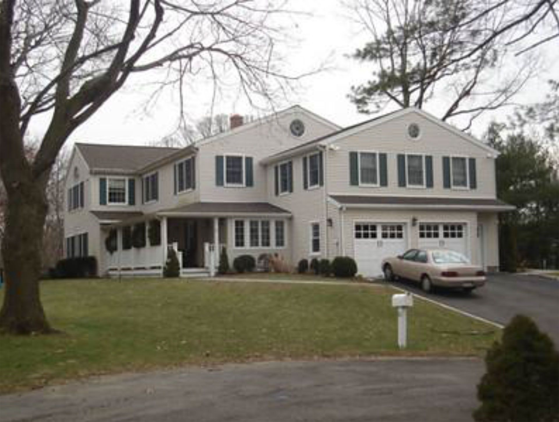 Two-story beige house with green shutters, a car in the driveway, and a lawn.