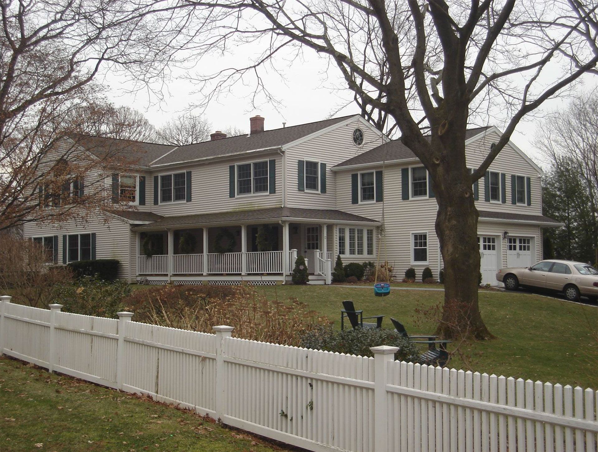 White two-story house with a porch and white picket fence in front; a car sits in the driveway.