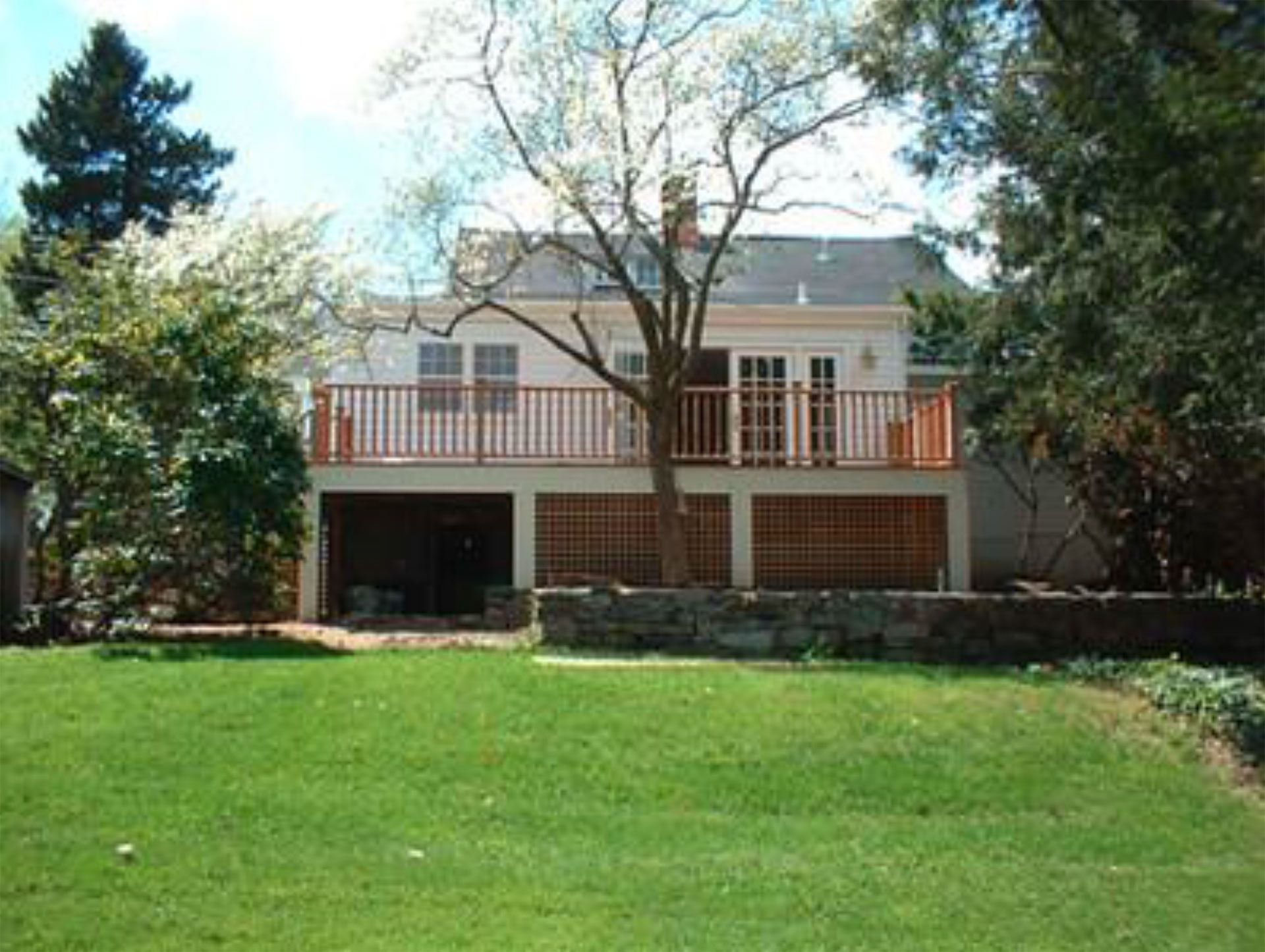 Backyard view of a house with a raised deck, featuring French doors and a tree growing through the deck. Green lawn.