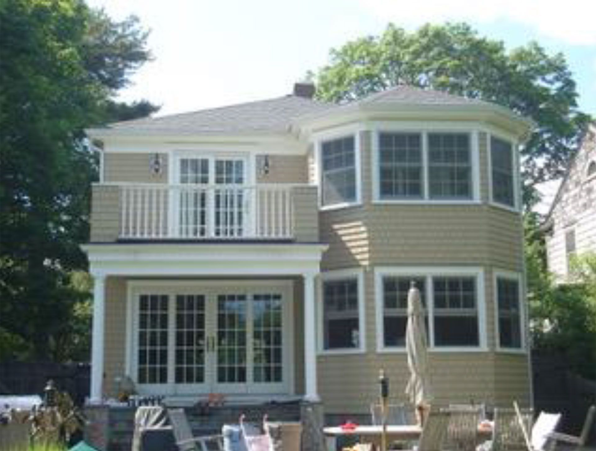 Two-story house with tan siding, double doors leading to a balcony, and a multi-paneled bay window.