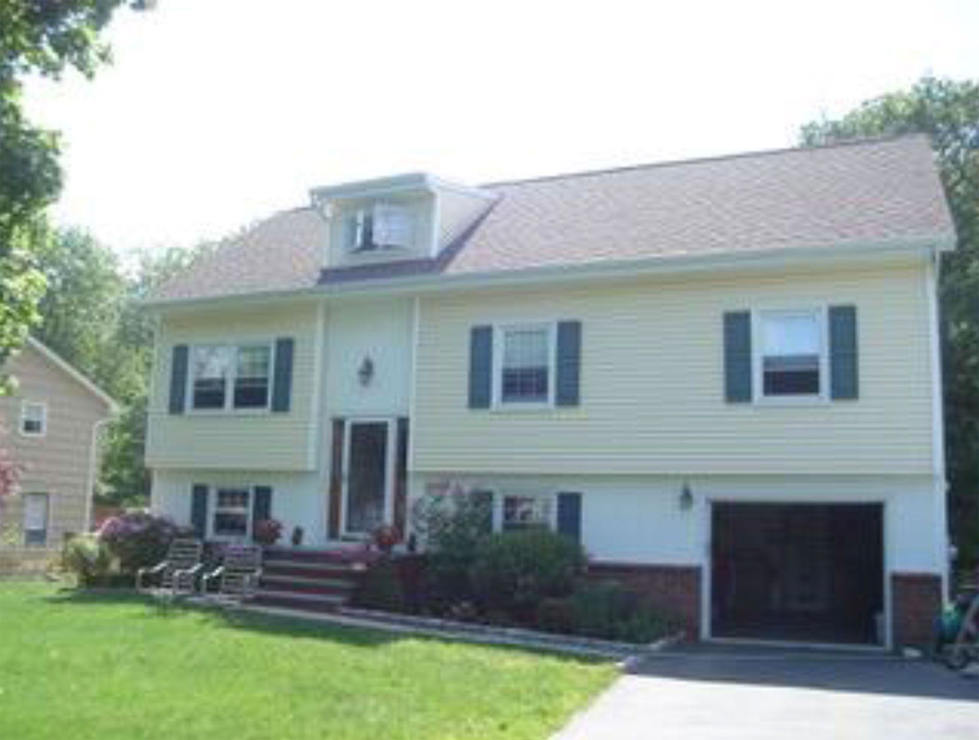 Two-story yellow house with green shutters, a garage, and a lawn.