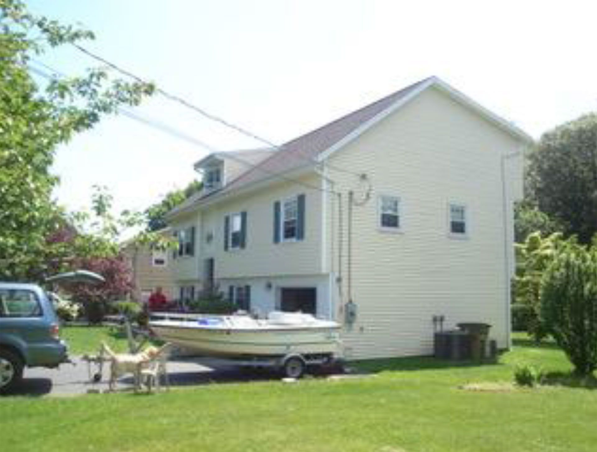 Two-story yellow house with boat in front, dog on lawn, blue SUV on left.