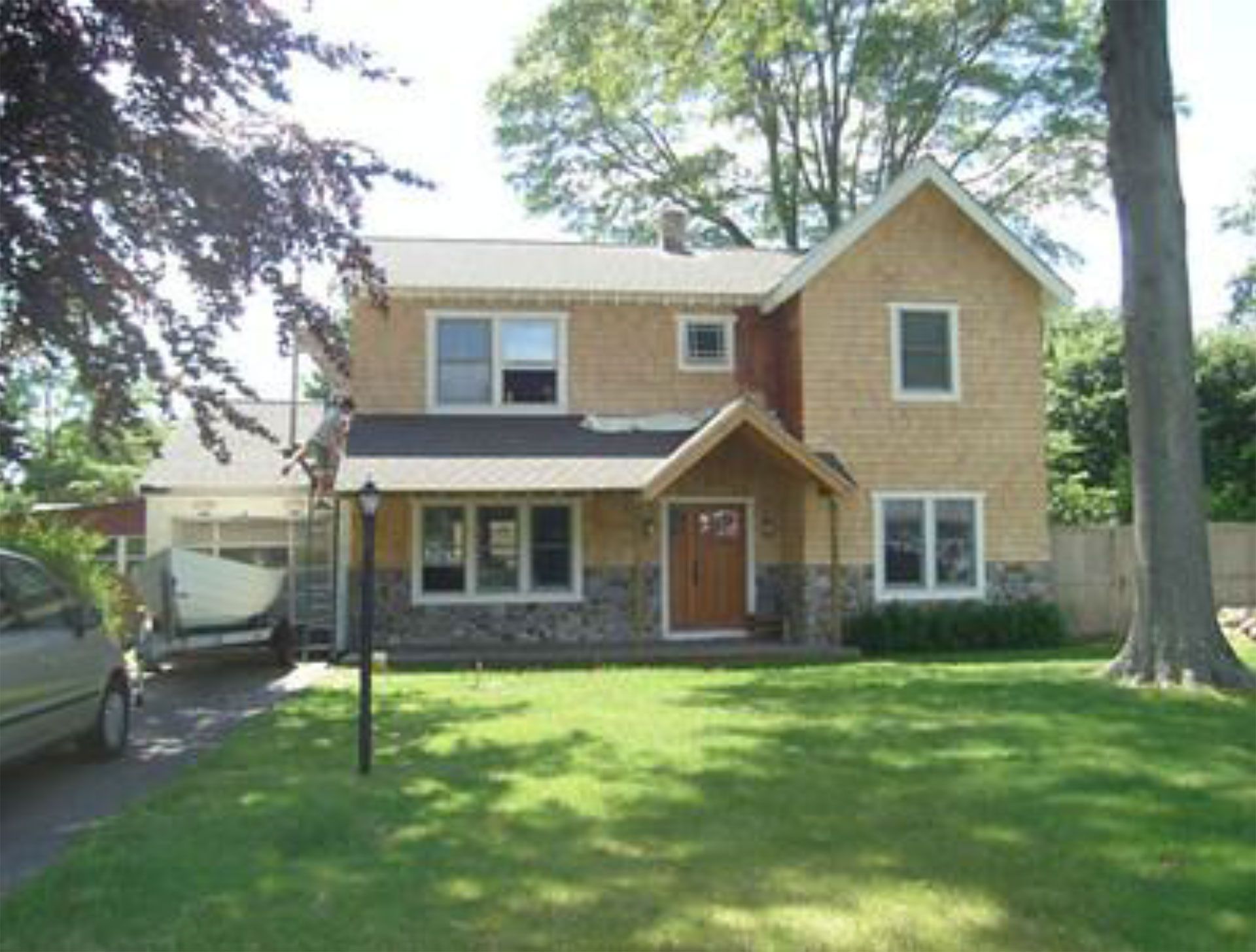 Two-story beige house with stone accents, a porch, and a boat parked in the driveway.