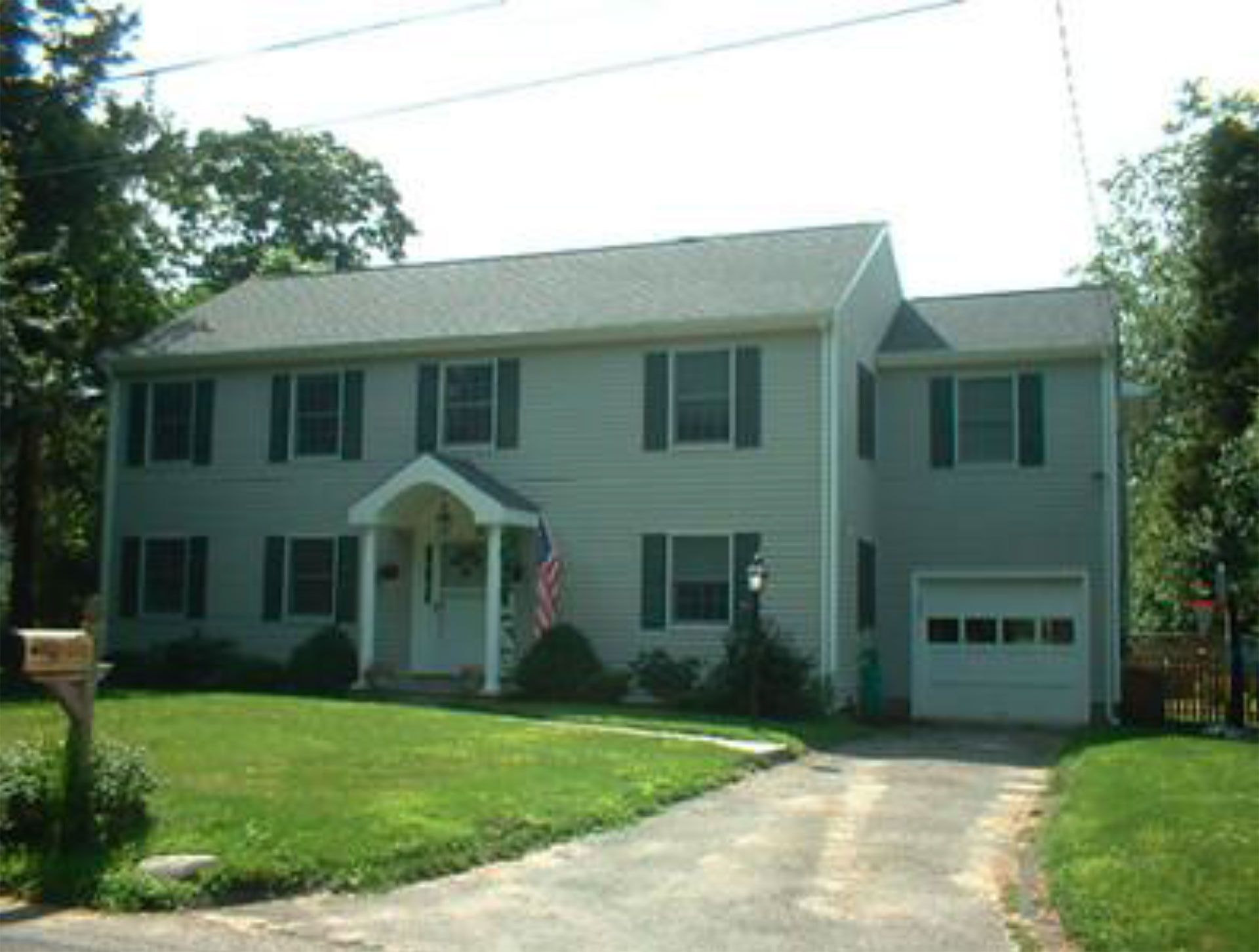 Two-story house with green shutters, a white garage door, and an American flag.