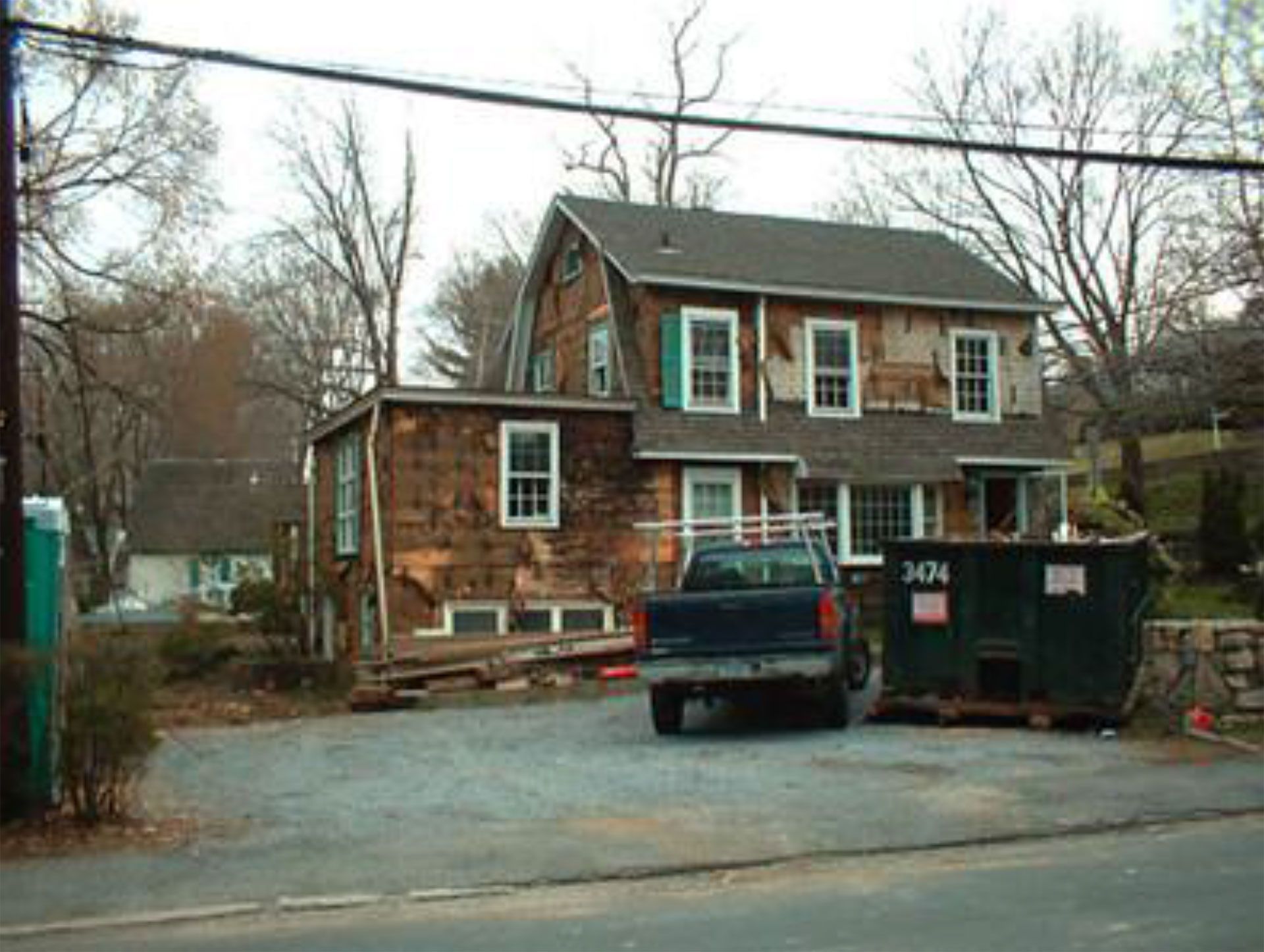 House under renovation with damaged siding, truck, and dumpster in front.
