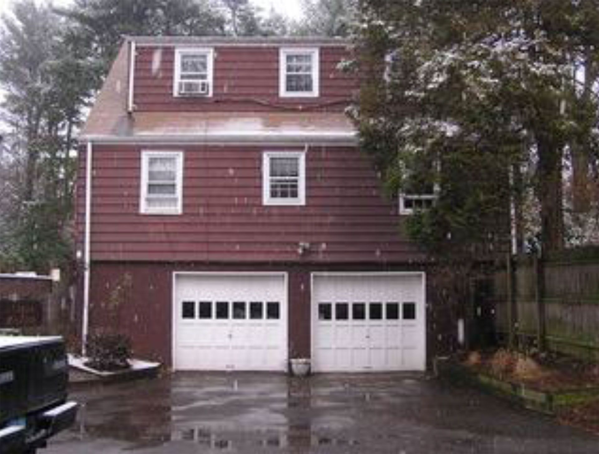 Two-story brick house with a two-car garage, white doors, and windows, driveway, with snow falling.