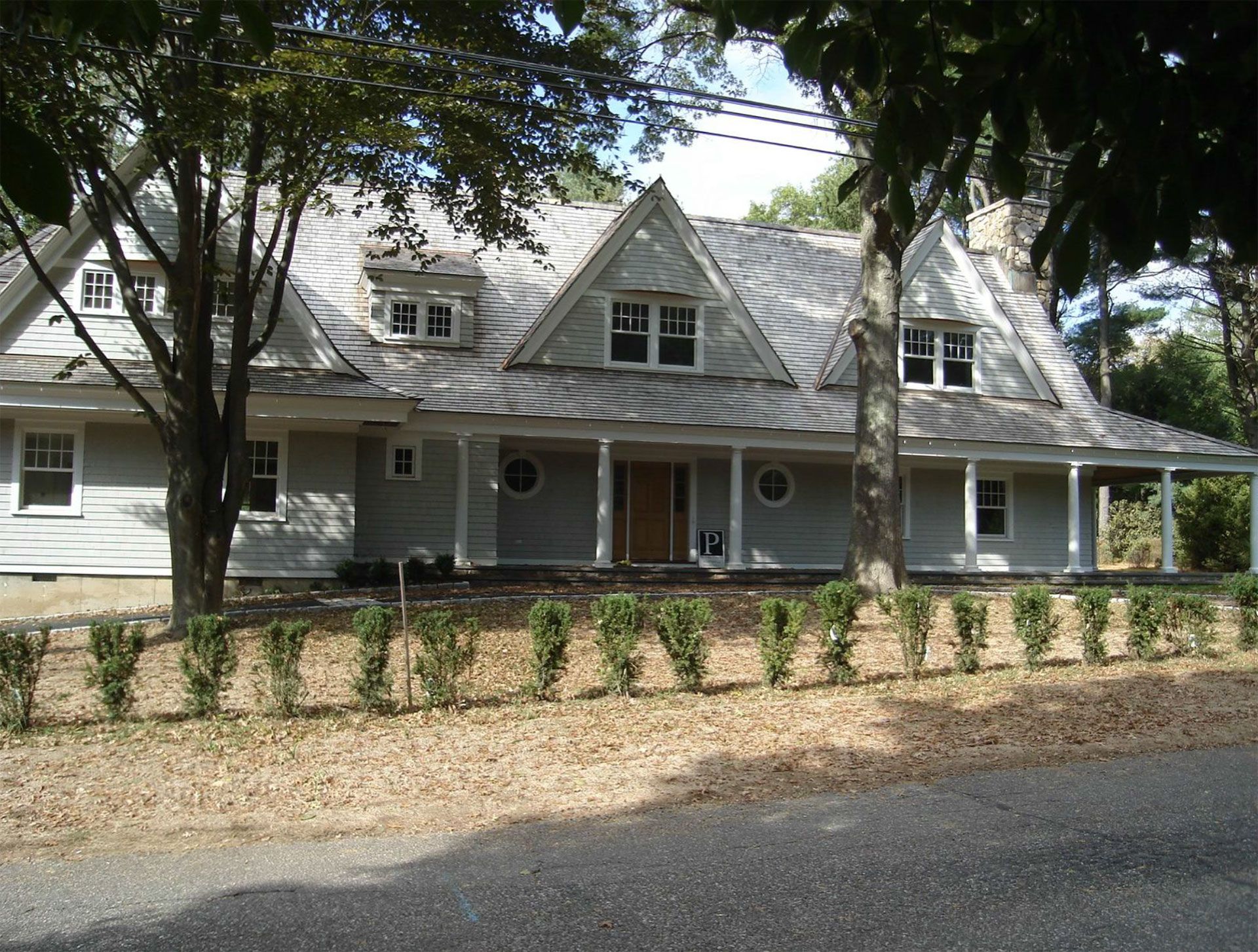 Light grey house with gabled roof, porch, and small bushes along the front.