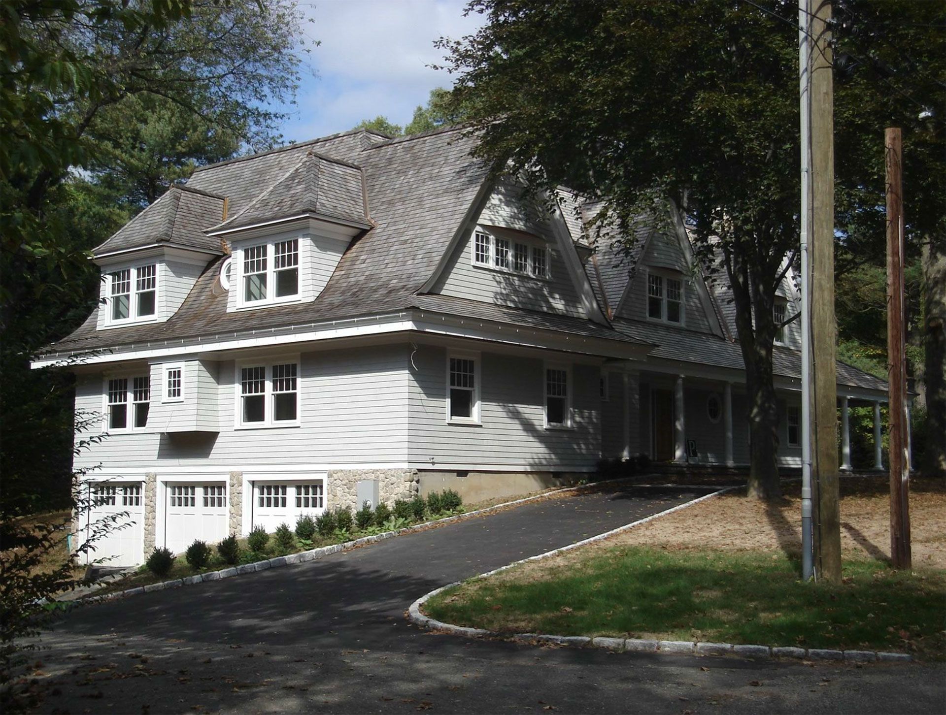 Gray house with gabled roof, dormers, and covered porch. Asphalt driveway.