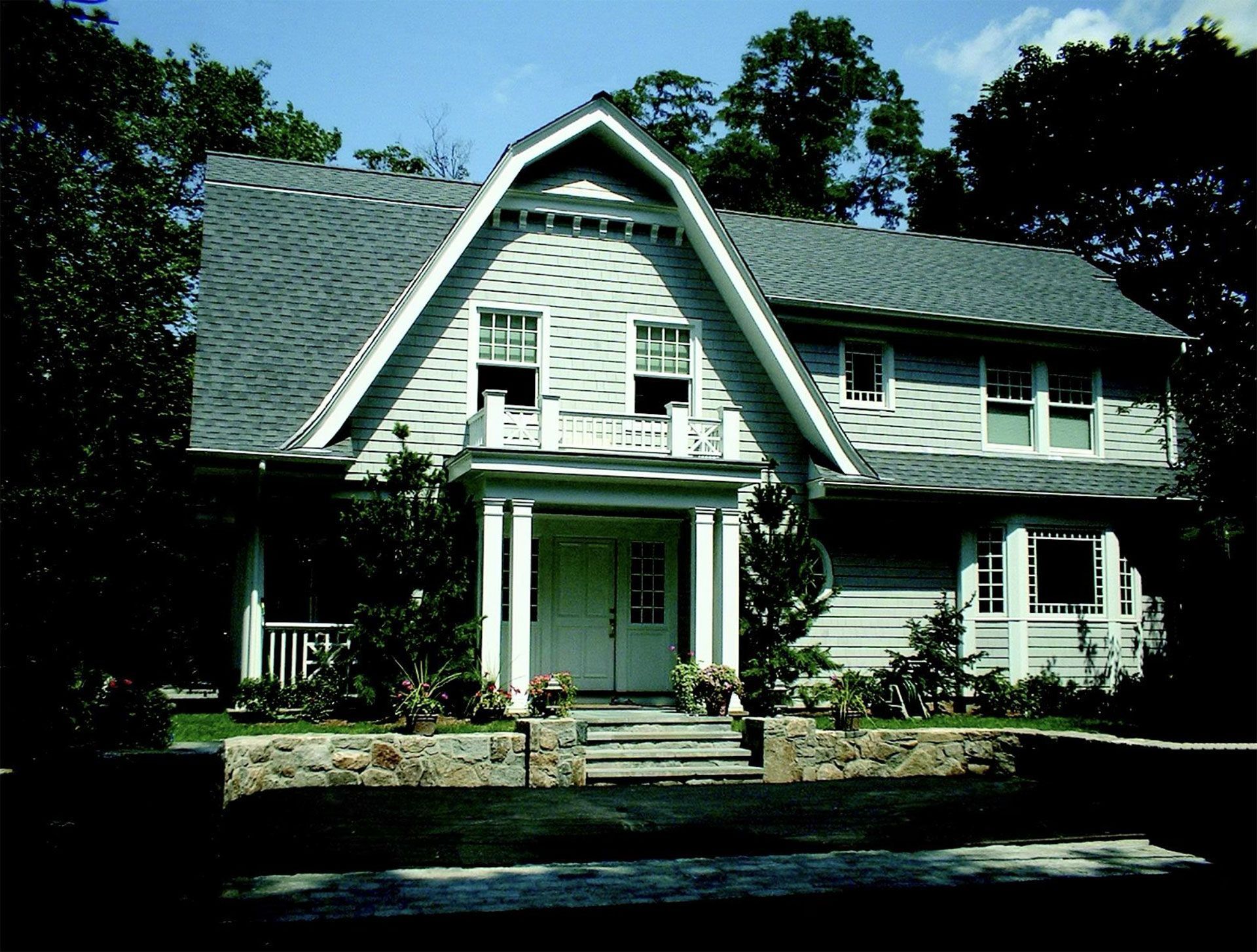 A two-story light gray house with a distinctive triangular gable and porch, set against trees.