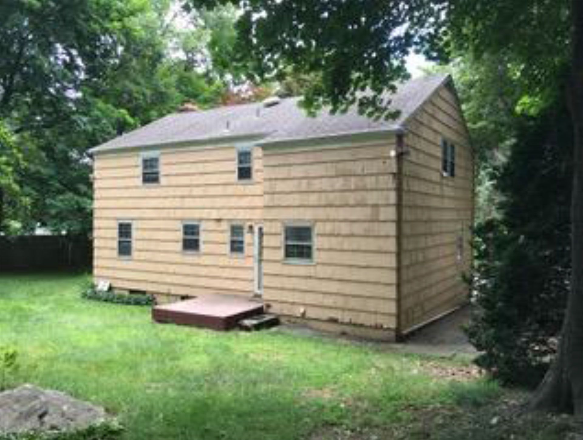 Back of a two-story house with light brown siding and several windows, in a grassy yard.
