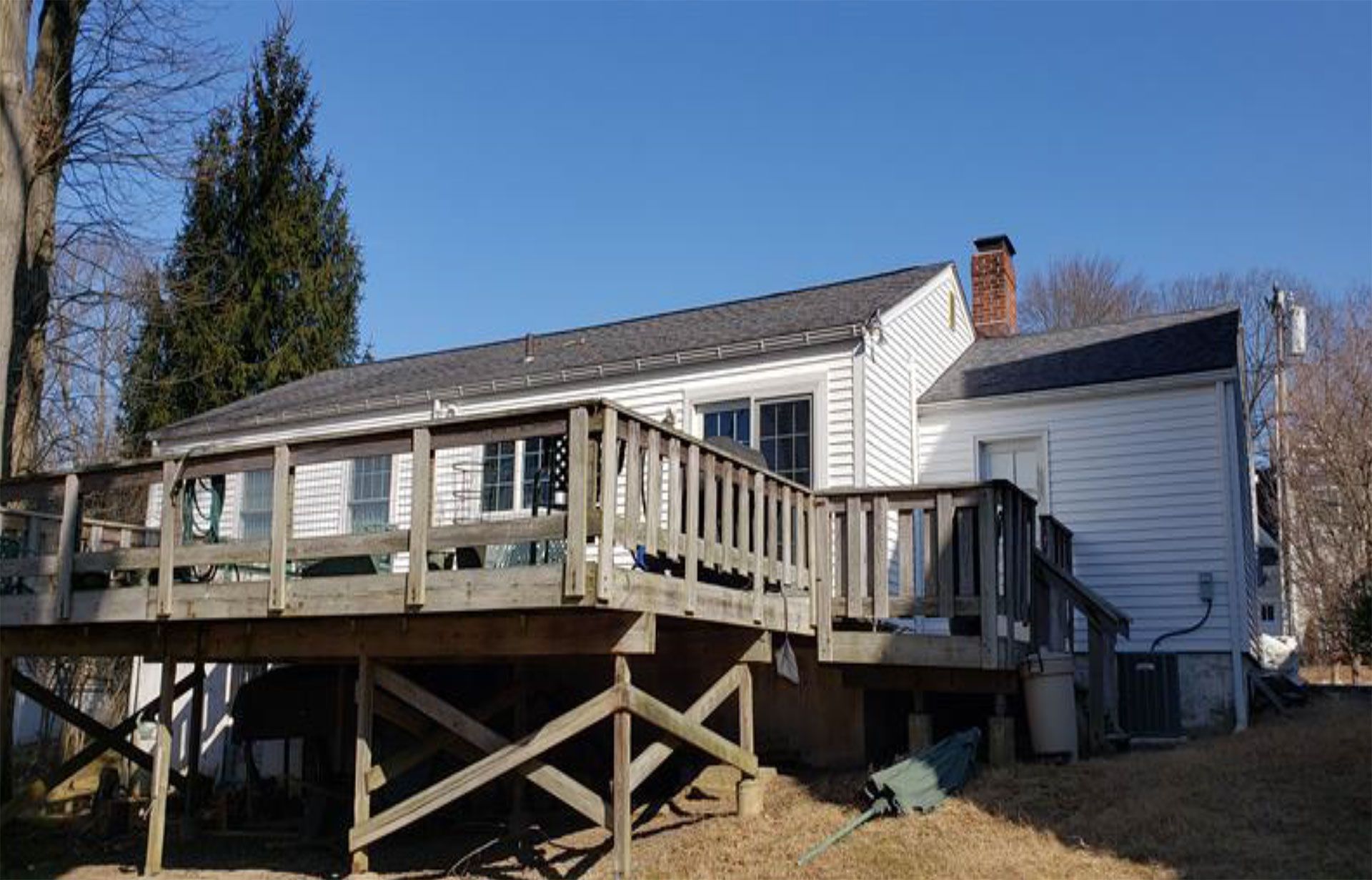 White house with a wooden deck, a chimney, and a clear blue sky.