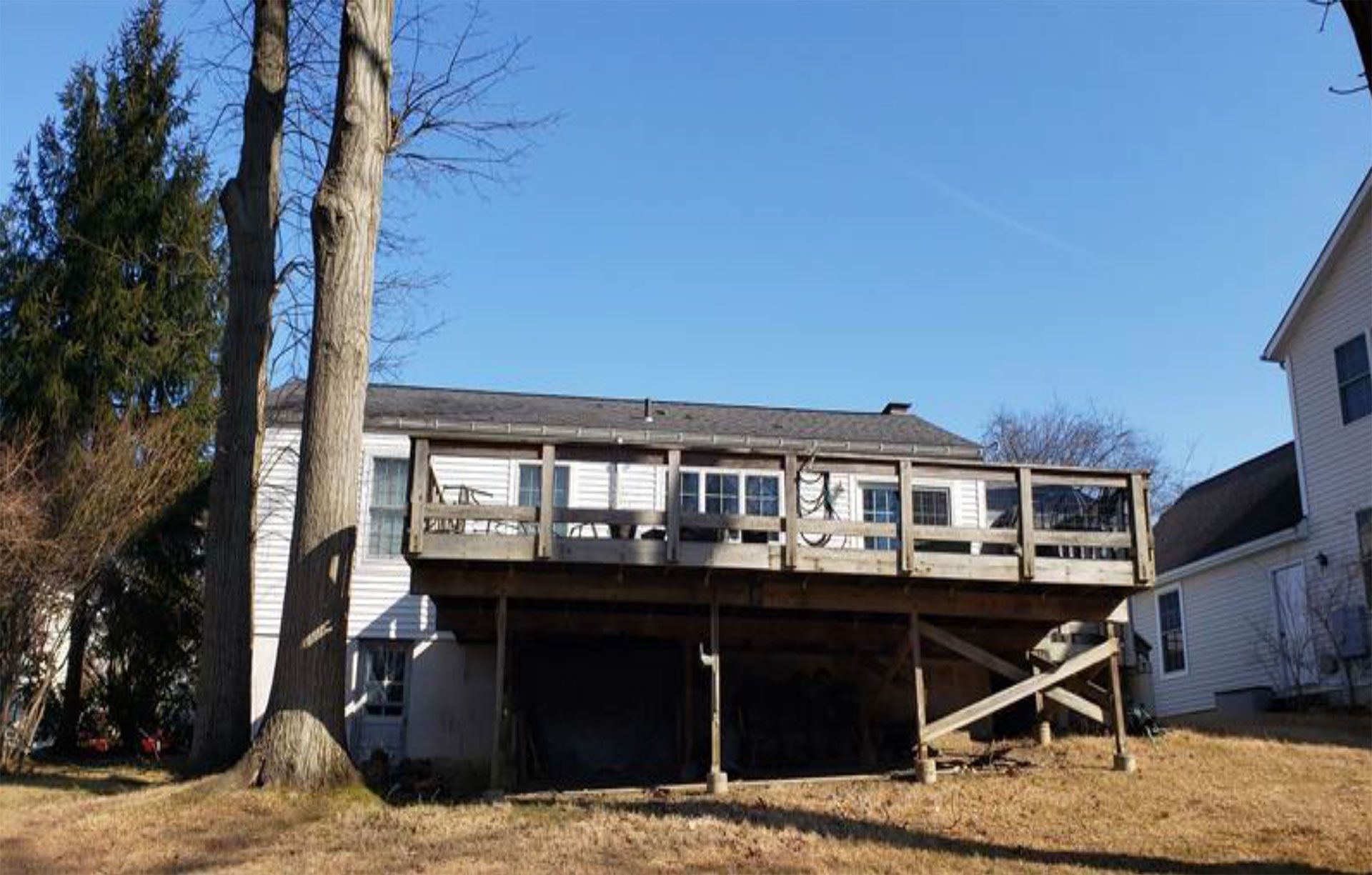 Two-story house with wooden deck, supported by posts. Blue sky, leafless trees.