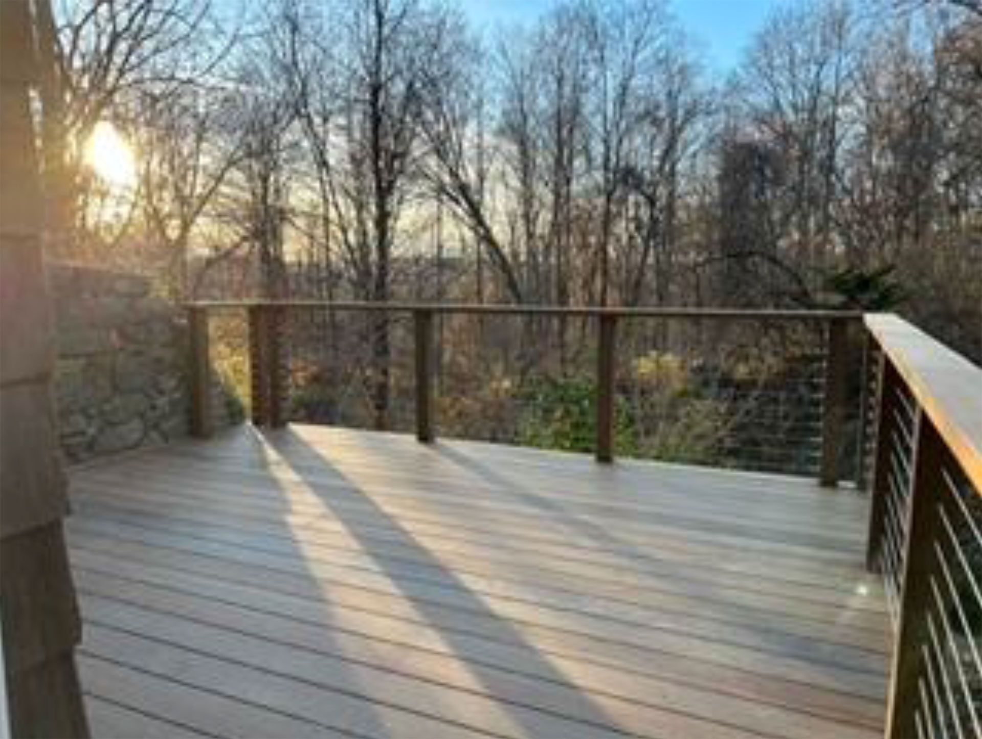 Wooden deck with cable railings overlooks trees at sunset.