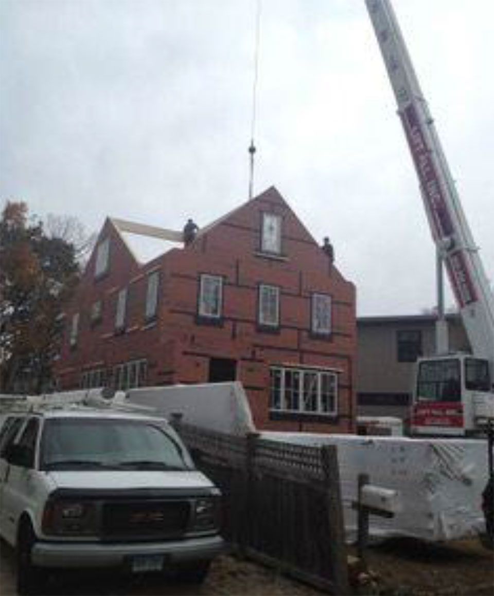 Construction site: brick house under construction, crane lifting materials. White van parked in front.