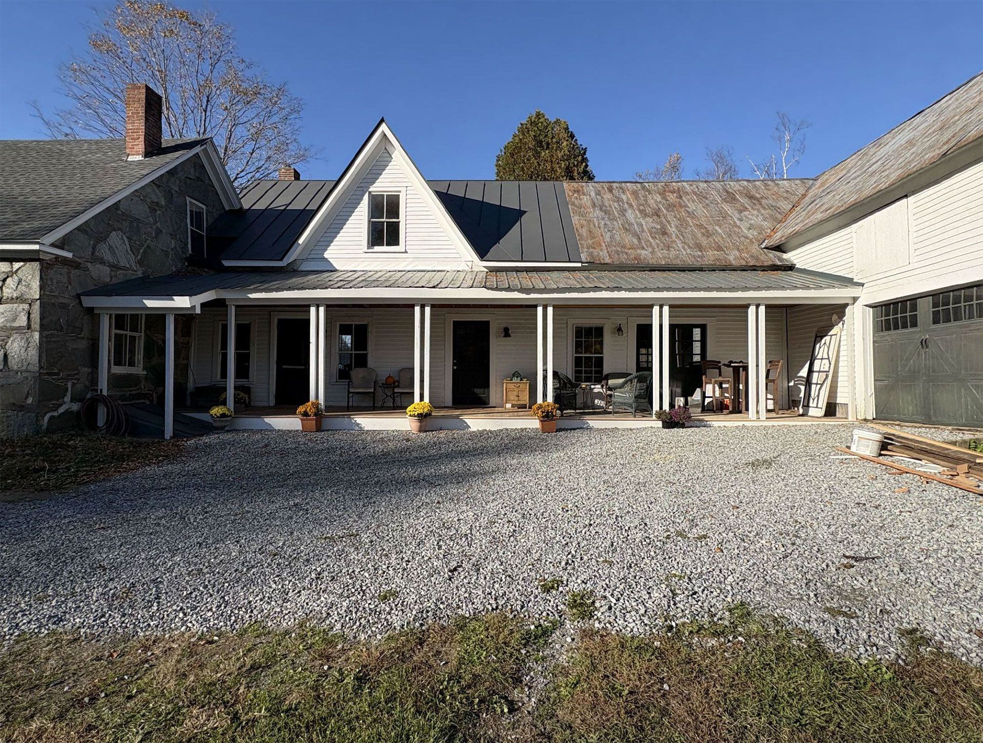A weathered farmhouse with a long porch, gravel driveway, and a clear, sunny sky.
