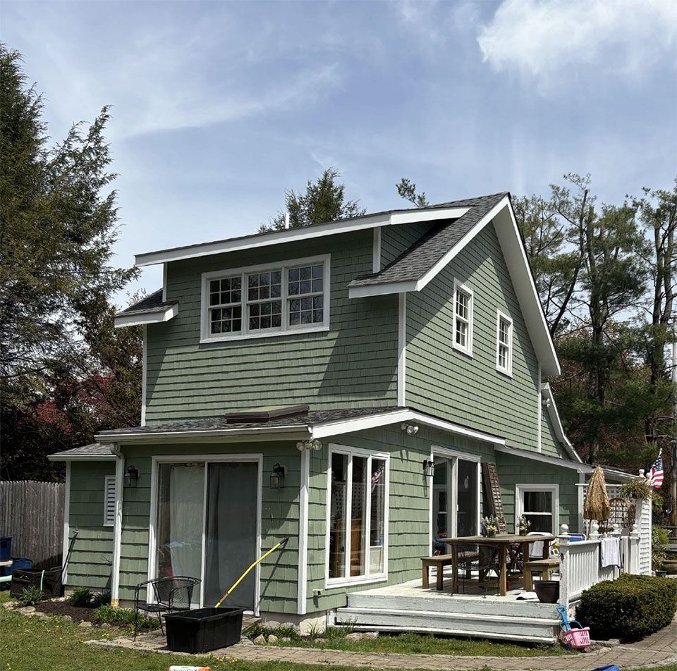Green two-story house with white trim, deck, and a cloudy blue sky.