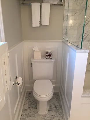 A small, white bathroom with a toilet, towels, and marble-like floor.