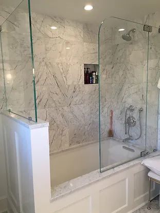 A white-tiled bathroom with a glass shower enclosure over a bathtub.