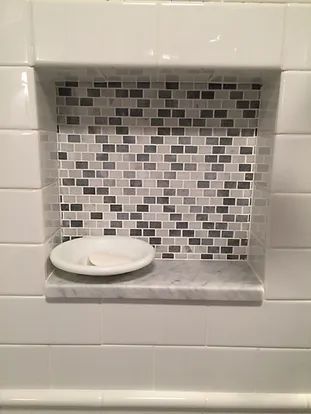 Tile-lined shower niche with mosaic tile back, marble shelf holding a white soap dish.