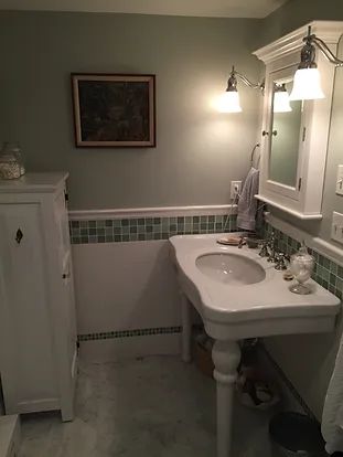 Bathroom with pedestal sink, white cabinet, green tile, and framed artwork.