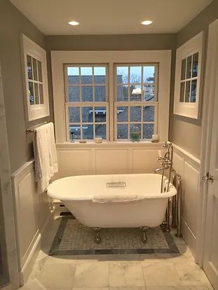 Bathroom with clawfoot tub beneath a window, white trim, light gray walls, and marble flooring.