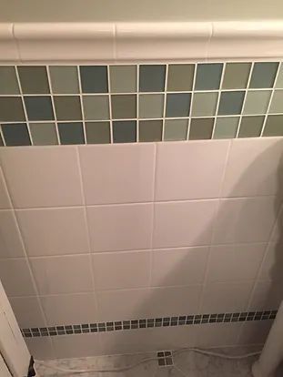 Bathroom wall with white tiles, a green and gray mosaic border, and decorative upper border.