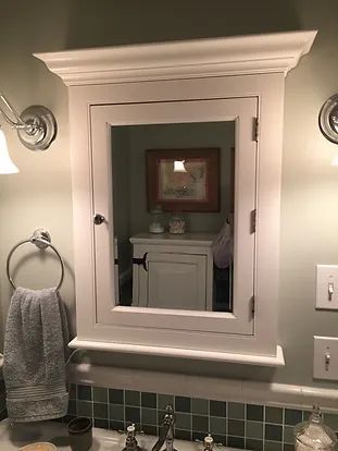 White medicine cabinet with mirror in bathroom, flanked by lights, towel ring, and switches.
