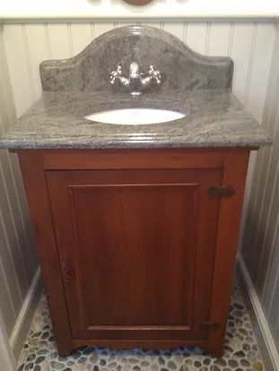 Wooden vanity with granite countertop and oval sink, set against a pebbled floor and paneled wall.