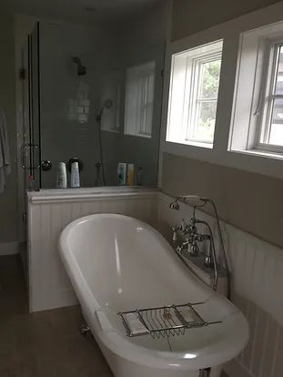 White clawfoot bathtub and glass shower in a bathroom with a window.
