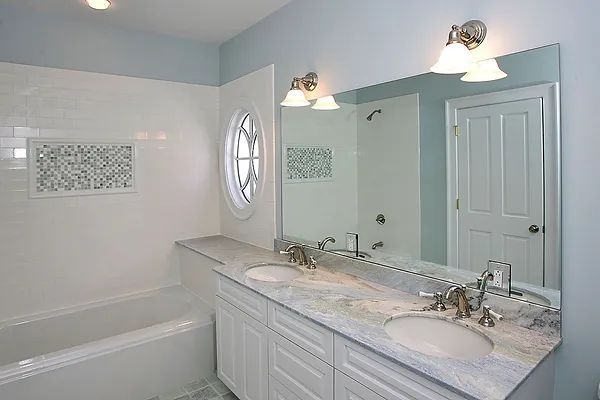 Bathroom with white cabinetry, a large mirror, a bathtub, and light blue walls.