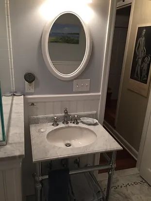 Bathroom with oval mirror, marble sink, silver fixtures, and light blue walls.