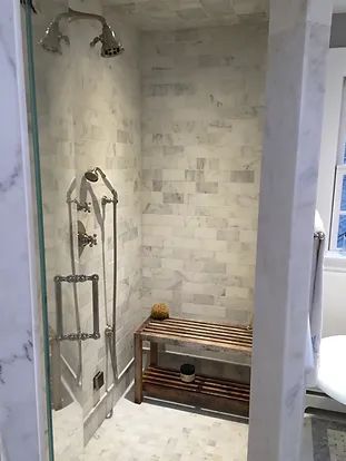 Marble-tiled shower with a wooden bench, glass door, and silver shower fixtures.