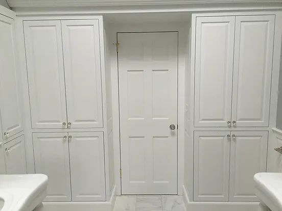 White bathroom with built-in cabinets flanking a white door.