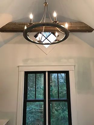 Chandelier hanging above a window with black trim, in a room with a rustic wooden beam.