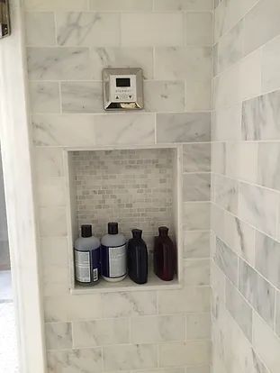 Shower with marble tile and a shampoo/soap niche holding bottles. A control panel is above the niche.