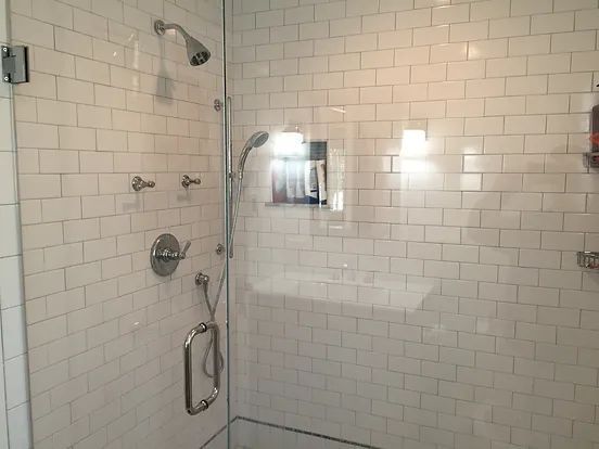 White-tiled shower with glass door, silver fixtures, and a handheld showerhead.