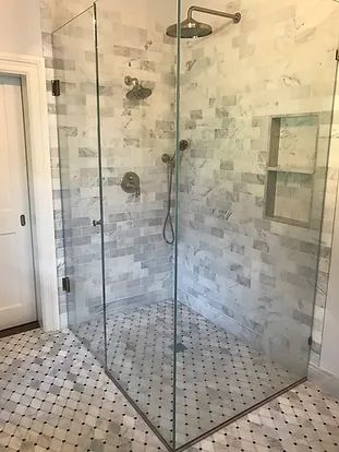 Glass-walled shower with marble tile walls and floor, set in a bathroom with white door.