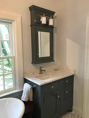 Dark blue bathroom vanity with marble countertop, mirror, and window.