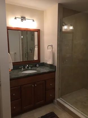 Bathroom with wooden vanity, green countertop, large mirror, and glass shower.
