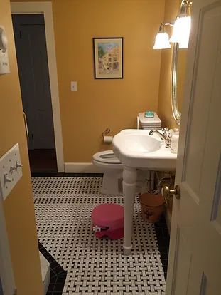 Small bathroom with pedestal sink, patterned tile floor, mustard yellow walls, and a pink step stool.