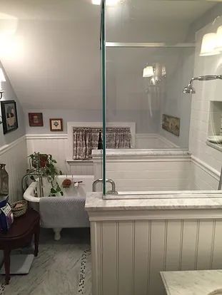 Bathroom with clawfoot tub, marble, white wainscoting, shower, and a glass partition.