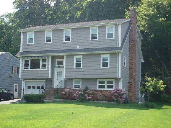 Gray two-story house with white trim, a brick chimney, and a garage on a grassy lawn.