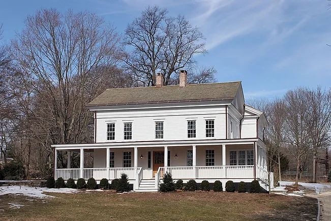 White two-story house with porch. Bare trees and blue sky background.