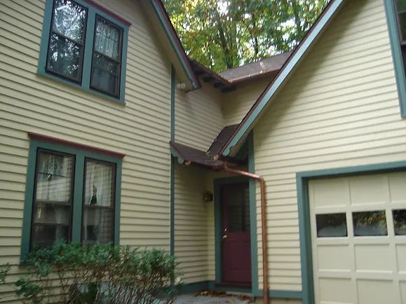 Yellow house with green trim, brown roof, and a red door. A garage door is to the right.