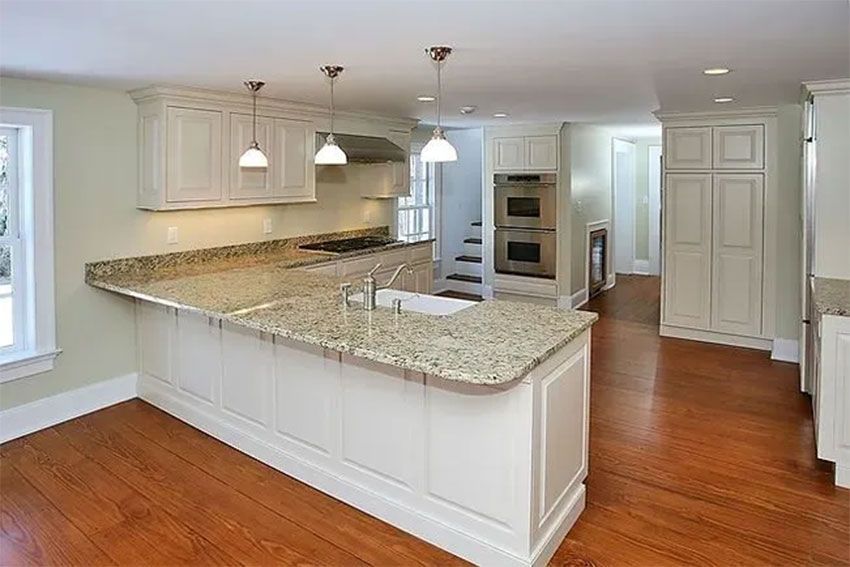 Spacious white kitchen with wood floors, granite countertops, and stainless steel appliances.