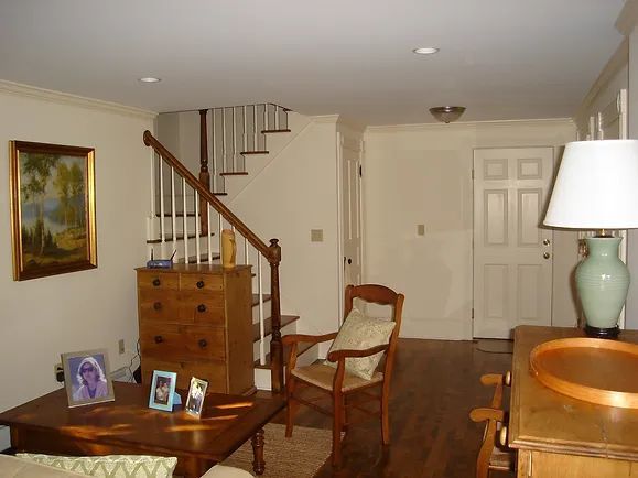 Living room with staircase, wooden furniture, artwork, and a lamp.